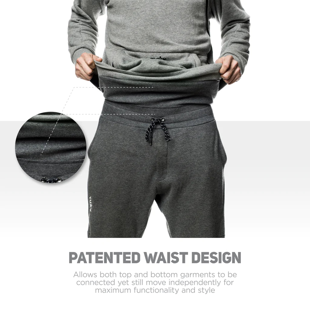 Tuxy suit zoomed in on the mid part of users body. User us pulling the tuxy suit up at the waist to show the one-piece component. The tuxy suit has dark grey pants on the bottom and light grey sweater on top. There is detailed writing on image describing the patented waist design. 